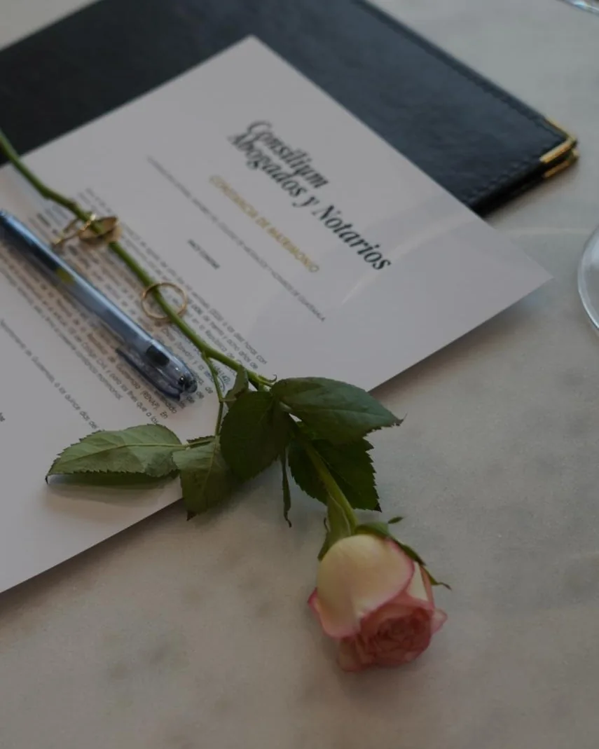 Constancia de matrimonio de Consilium sobre una mesa de mármol, junto a los anillos y una rosa.